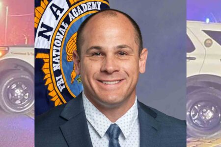 Major Dustin Burlison in professional attire, standing in front of an FBI National Academy banner.