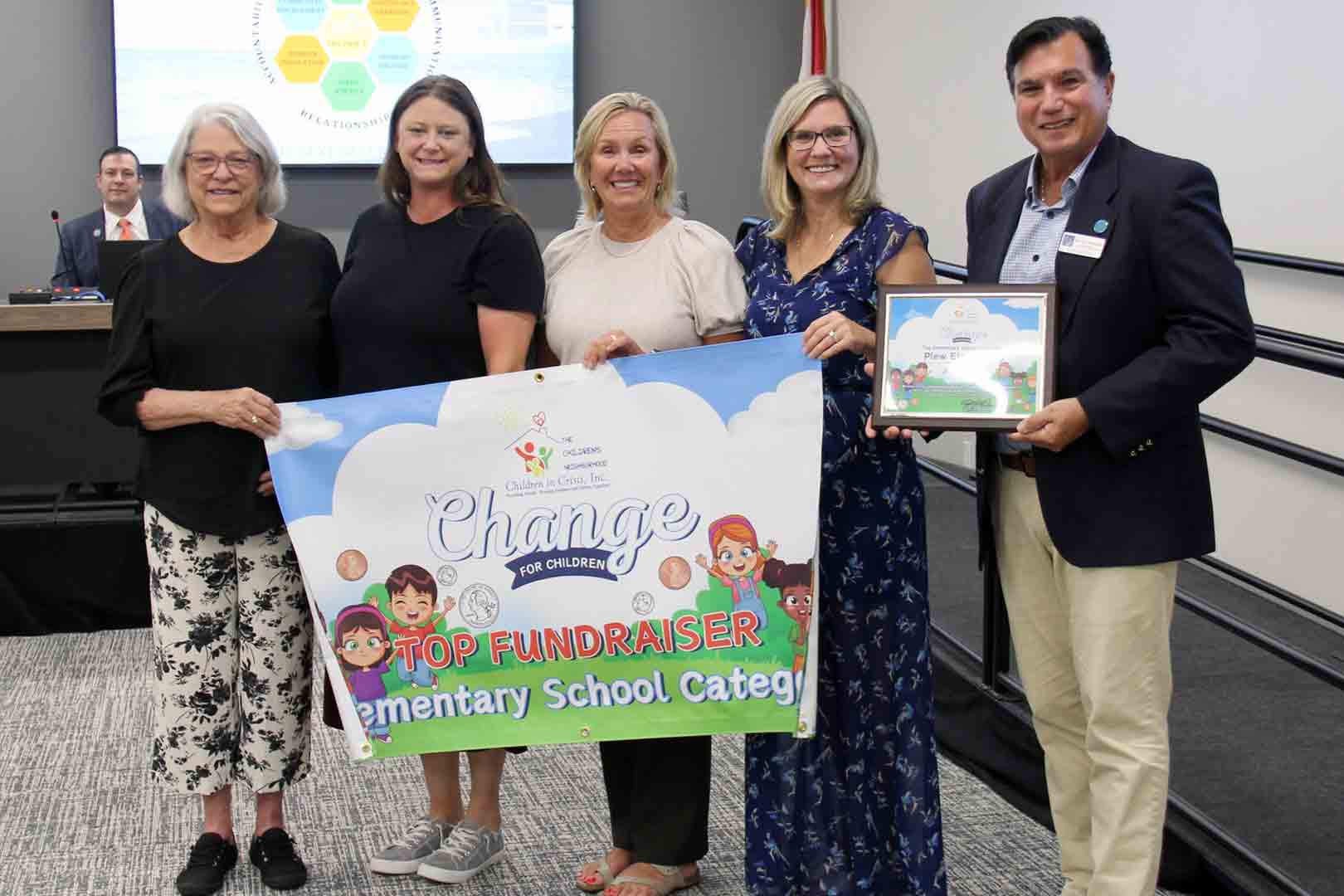 Five people holding an Elementary School Top Fundraiser banner at a school board meeting
