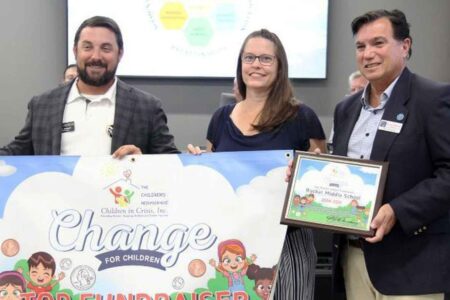 Three people holding a "Change for Children" Top Fundraiser banner at a school board meeting