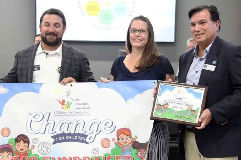 Three people holding a "Change for Children" Top Fundraiser banner at a school board meeting