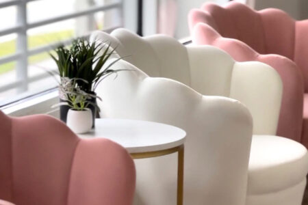 Pink and white chairs with a round table and potted plant at Blush Beauty Lounge.
