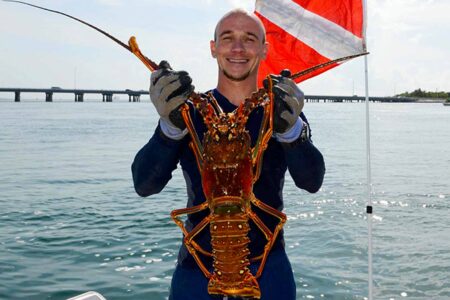 Diver holding a large Florida spiny lobster on a boat with a dive flag in the background
