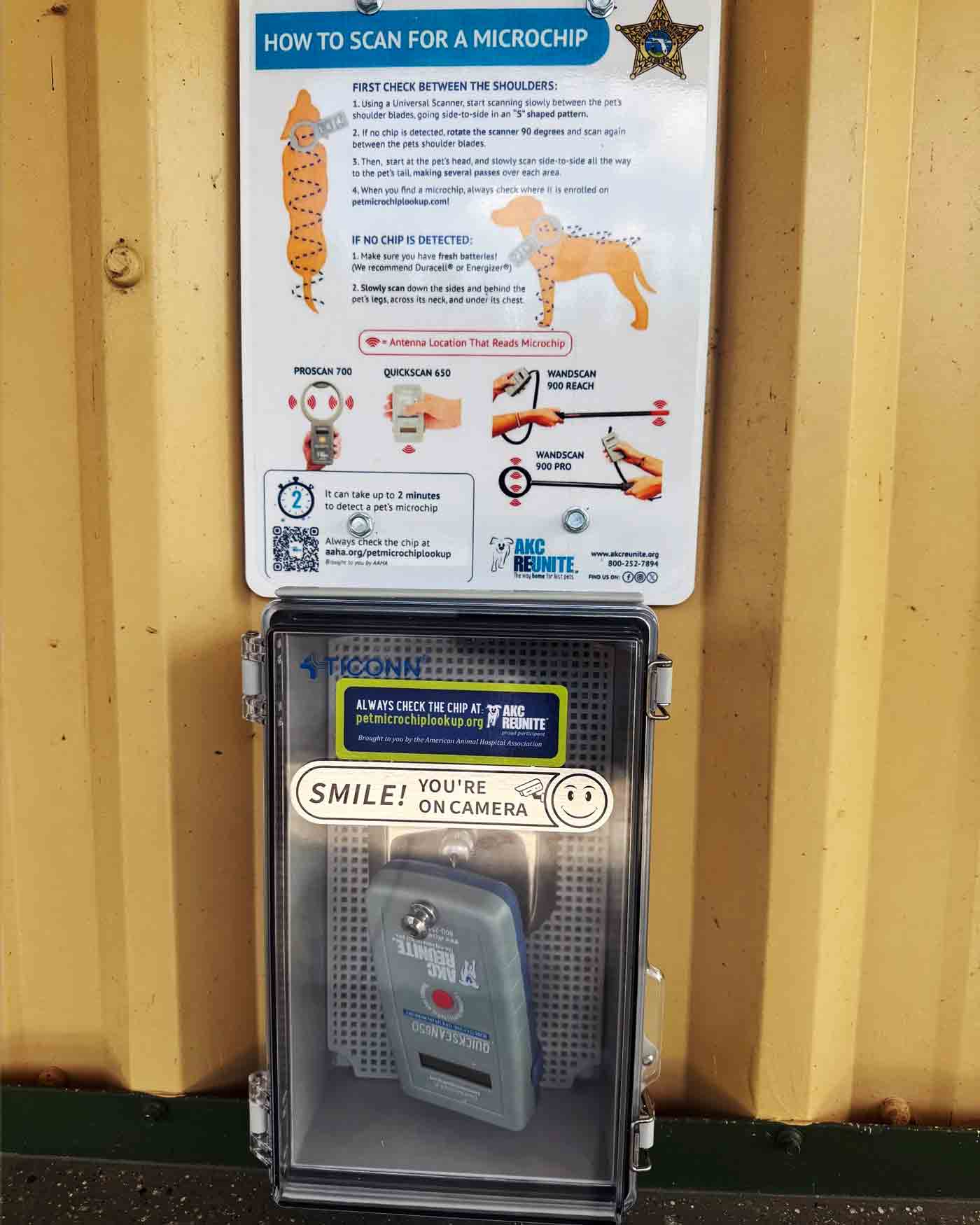 Wall-mounted pet microchip scanner box with camera warning and AKC Reunite label.