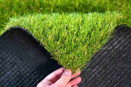 Hand lifting a section of synthetic turf to show backing
