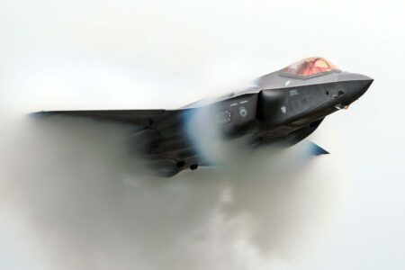 F-35 Lightning II fighter jet flies through a vapor cloud during a maneuver.