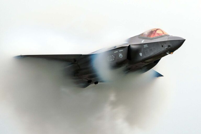 F-35 Lightning II fighter jet flies through a vapor cloud during a maneuver.