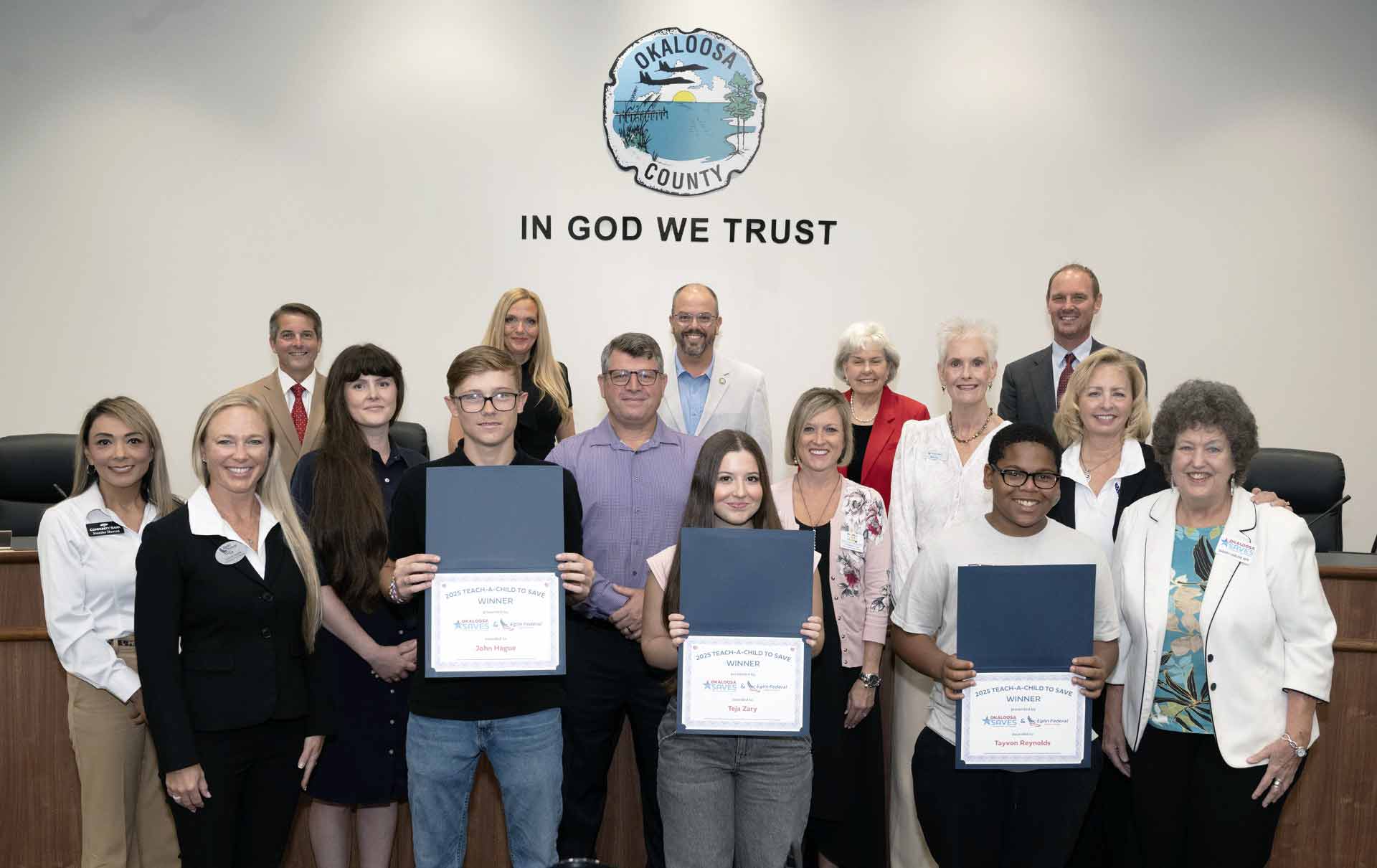 Three student winners pose with certificates and community leaders during a Teach Children to Save recognition event in Okaloosa County.
