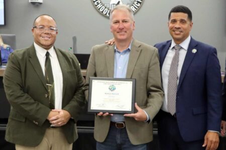 Nathan Basnett holds his Volunteer of the Year certificate flanked by Addie R. Lewis School Principal Dr. Nathaniel Chatman and Superintendent Marcus Chambers.