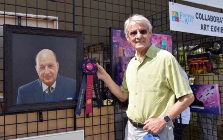 Man holding award ribbon next to portrait painting at Festival of the Arts.
