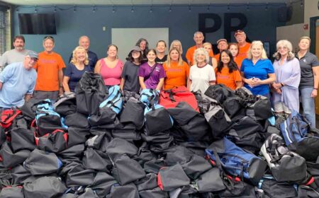 Large group of volunteers stand behind hundreds of Bags of Hope for foster children in Northwest Florida.