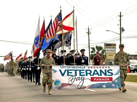 Members of the military and honor guard lead the City of Niceville Veterans Day Parade carrying U.S. and service flags.