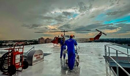 Medical crew pushes stretcher toward life flight helicopter on hospital rooftop.