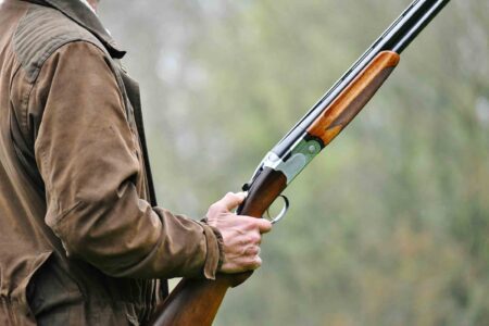 A hunter holding a shotgun outdoors in preparation for recreational hunting.