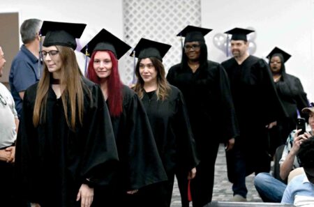 Adult graduates in black caps and gowns walk in procession during a Career Online High School graduation ceremony in Okaloosa County.