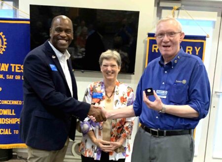 Rotary District Governor Andre Boyd presents a Paul Harris Fellow pin to Mid-Bay Bridge Rotarian John Suerken as Jan Pooley looks on.