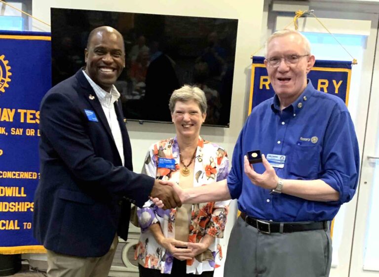 Rotary District Governor Andre Boyd presents a Paul Harris Fellow pin to Mid-Bay Bridge Rotarian John Suerken as Jan Pooley looks on.