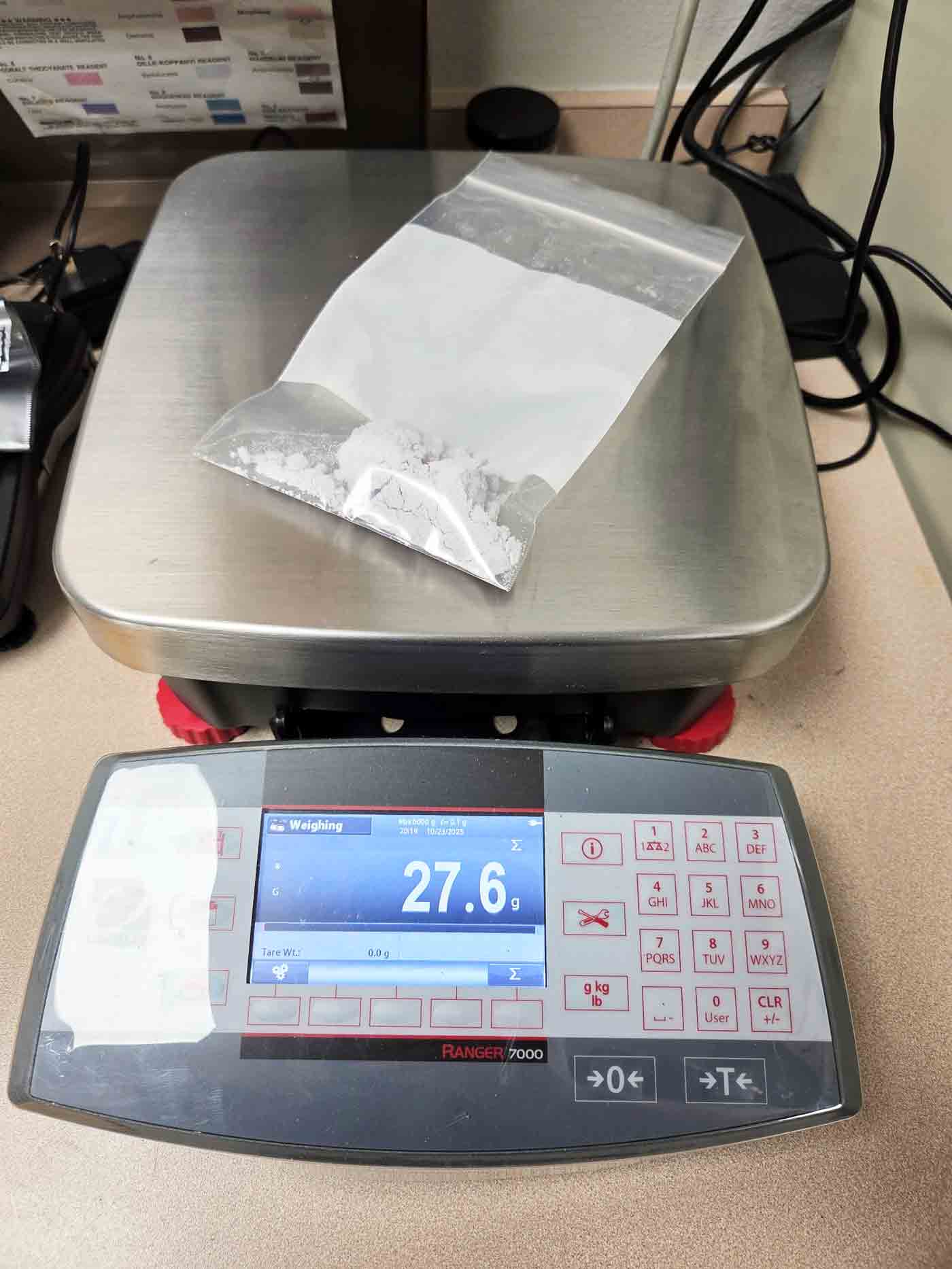 A clear plastic bag containing a white powdery substance on a digital scale reading 27.6 grams.