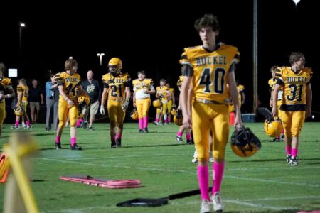 Ruckel Rams football players walk off the field under stadium lights during a night game at Eagle Stadium in Niceville, Florida.