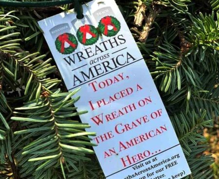 A Wreaths Across America tag tied to a holiday wreath branch.