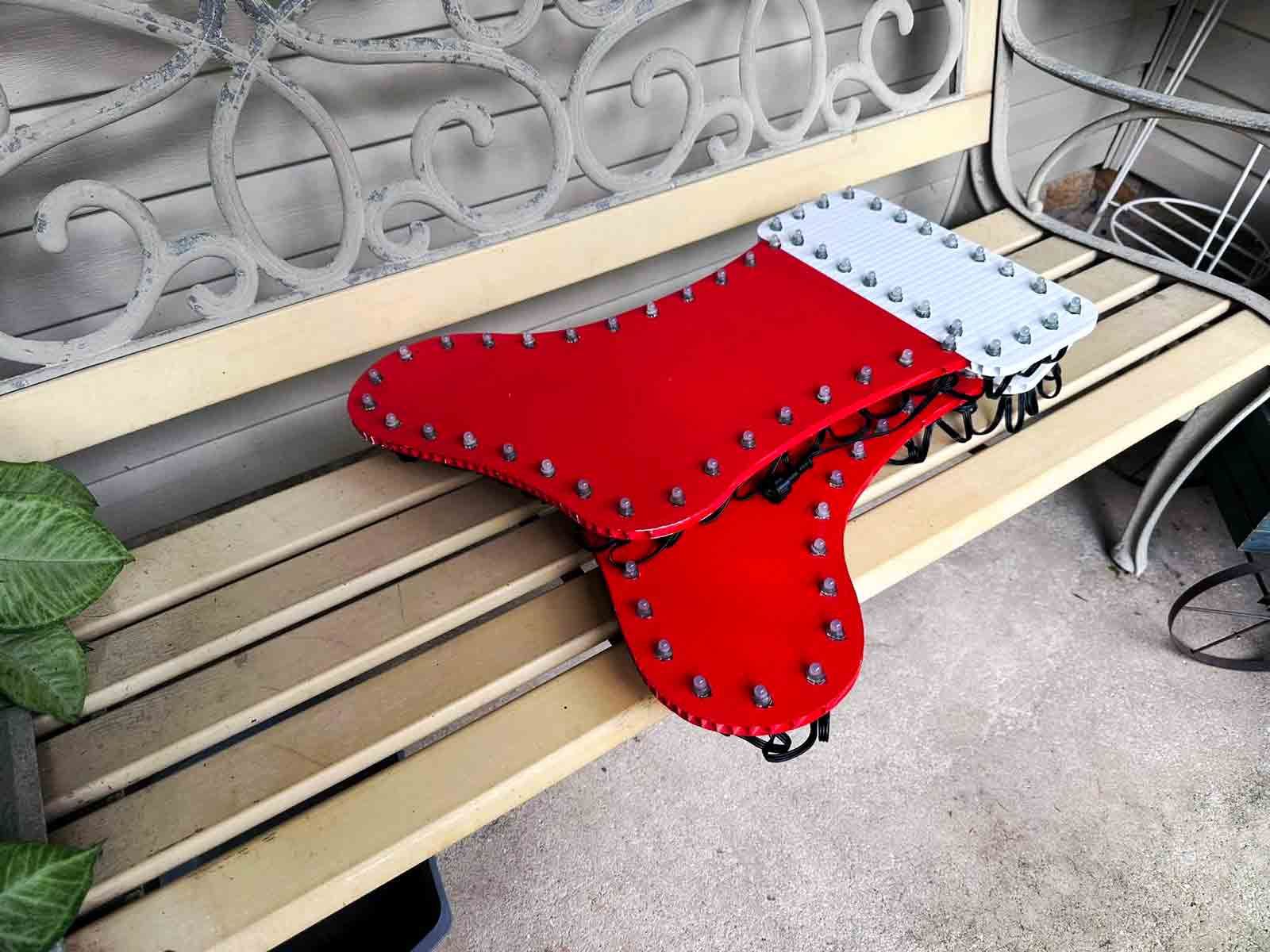 A red and white Christmas stocking-shaped light prop rests on a bench before setup for Geek Lights on the Corner.