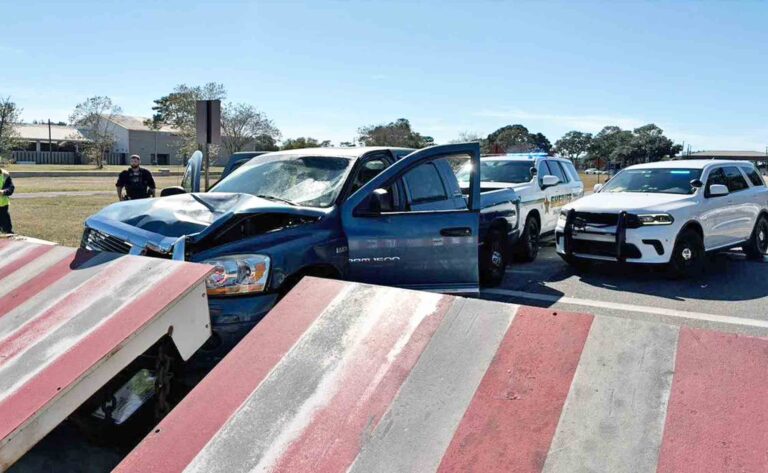 Damaged pickup truck after striking red and white barrier near an Eglin Air Force Base checkpoint, with OCSO vehicles behind it.