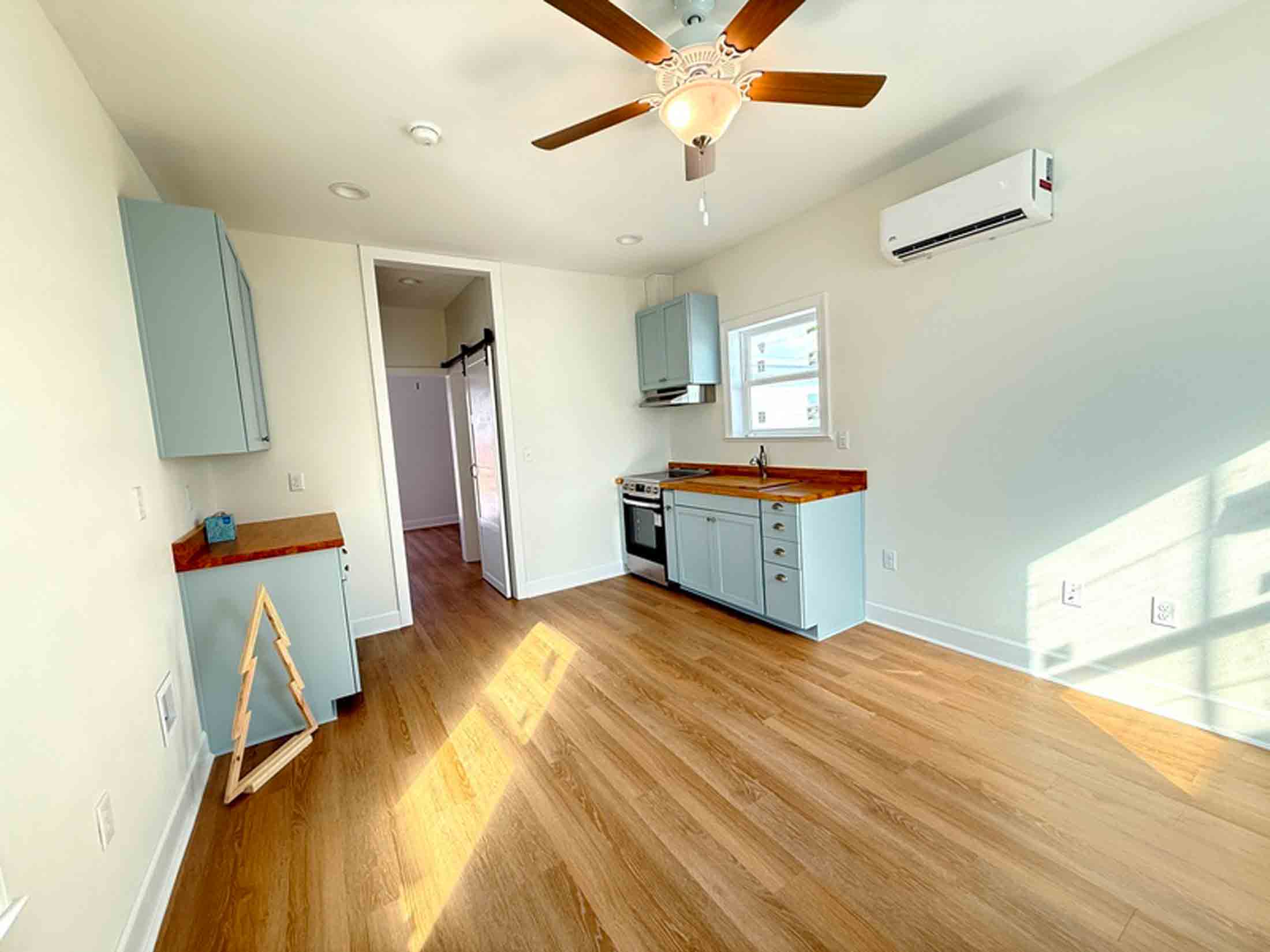 Interior of a student-built tiny home showing a compact kitchen with blue cabinets, wood countertops, and light wood flooring.