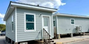 Two student-built tiny homes constructed by Okaloosa Technical College students, shown from the exterior with light gray siding and white trim.