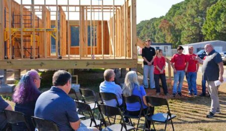 Fort Walton Beach High School Building Trades students and guests gather beside a student-built tiny house under construction during a project preview event.