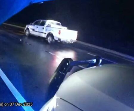 A white Ford F-150 pickup truck stopped on a wet Highway 98 at night with patrol lights visible in the foreground.