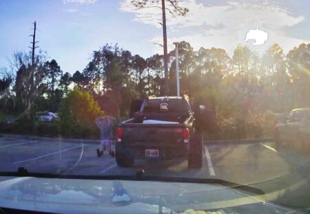 A sheriff’s deputy’s dash-camera view shows a person kneeling beside a black pickup truck during a traffic stop at sunset.
