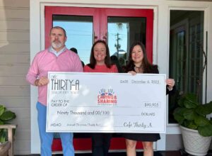 Representatives from Café Thirty-A and Caring and Sharing of South Walton hold a ceremonial check for $90,905 outside the restaurant in Seagrove Beach.