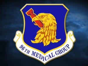 Emblem of the 96th Medical Group at Eglin Air Force Base featuring a golden eagle holding a red medical staff on a blue shield.