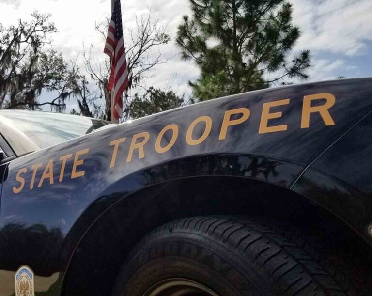 Close-up of a Florida Highway Patrol vehicle with “State Trooper” lettering visible and an American flag in the background.