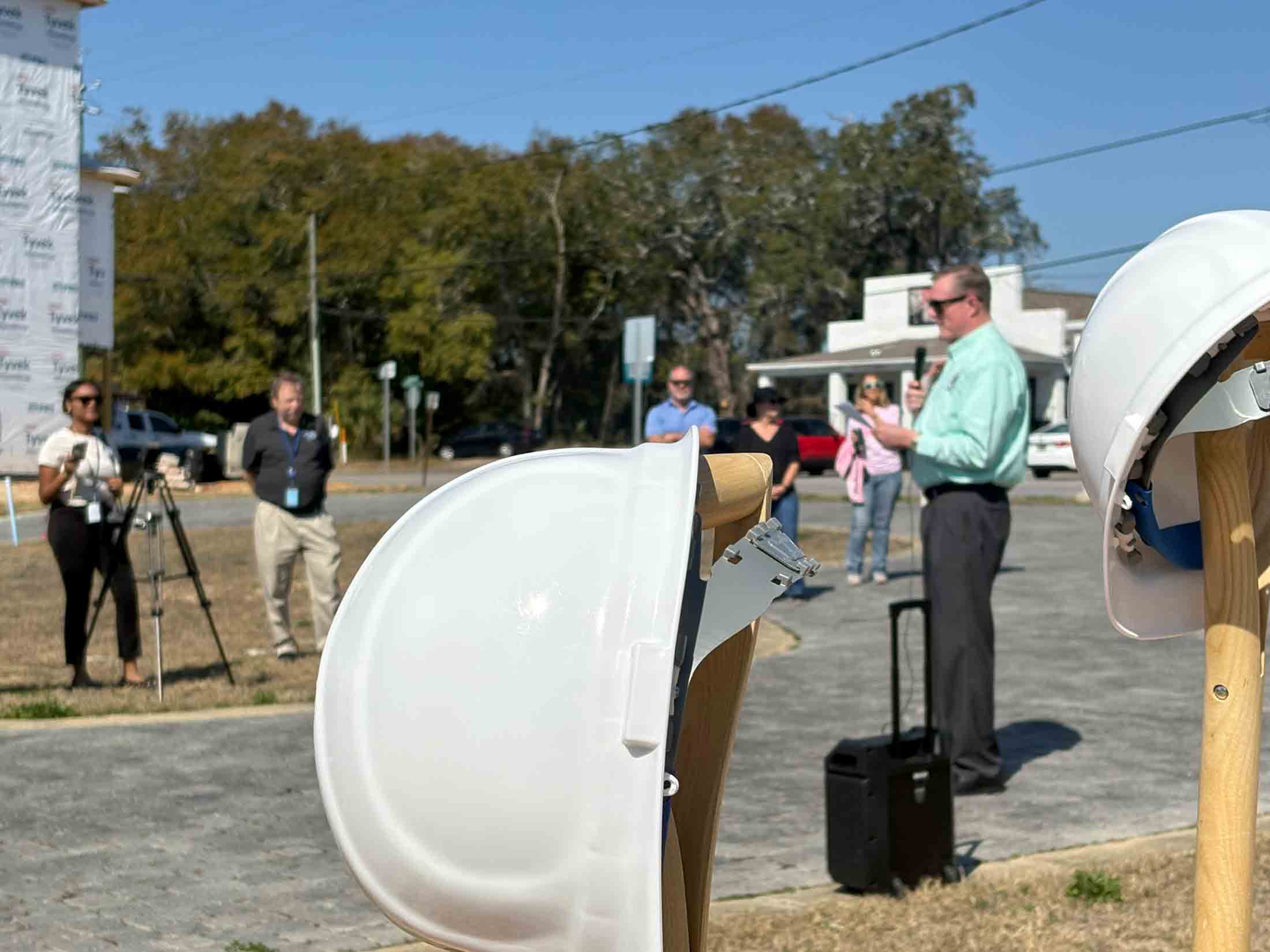 White ceremonial hard hats displayed in the foreground as Mayor Daniel Henkel speaks during the Old Town Landing dock and pier groundbreaking in Niceville.