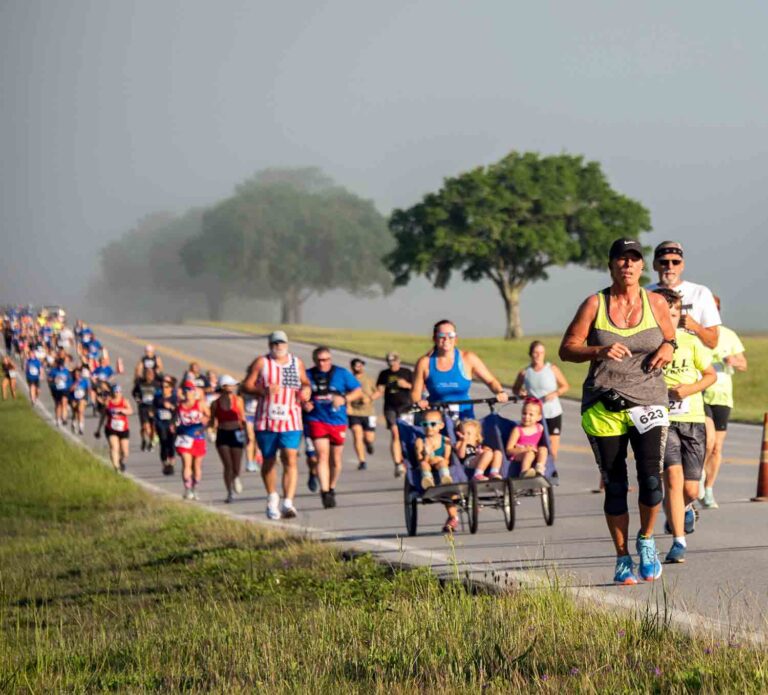 Participants run and walk along a roadway during the Eglin Gate-to-Gate Memorial Run/Walk, with multiple runners and walkers moving in a group across the base.