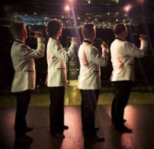 Four performers sing into microphones during a stage performance of the musical “Forever Plaid.”