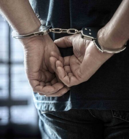 Person with hands behind back in handcuffs.