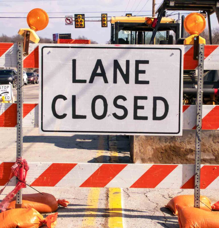 Road construction barricade with “Lane Closed” sign blocking traffic lane