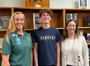 Bruner Middle School student Jake Revette stands with two educators in a school library.