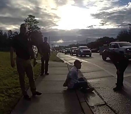 Deputies detain a man sitting on a curb during a traffic stop in Niceville as vehicles pass on a nearby roadway.