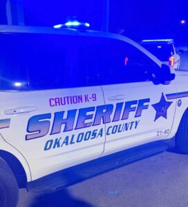Okaloosa County Sheriff’s Office patrol vehicle with blue emergency lights at night.