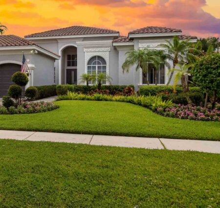 Free seminar to teach homeowners how to grow a better lawn Well-maintained Florida home with a lush green lawn, landscaped garden beds, and palm trees in the front yard.