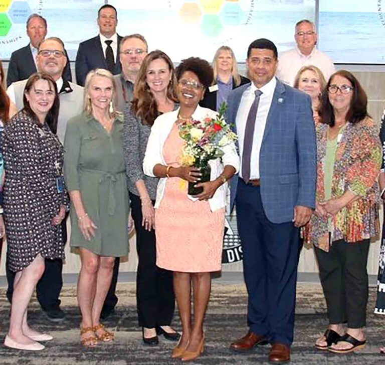 Duscha Ross stands with Okaloosa County School District leaders after being named Director of Secondary Education, holding a bouquet of flowers.