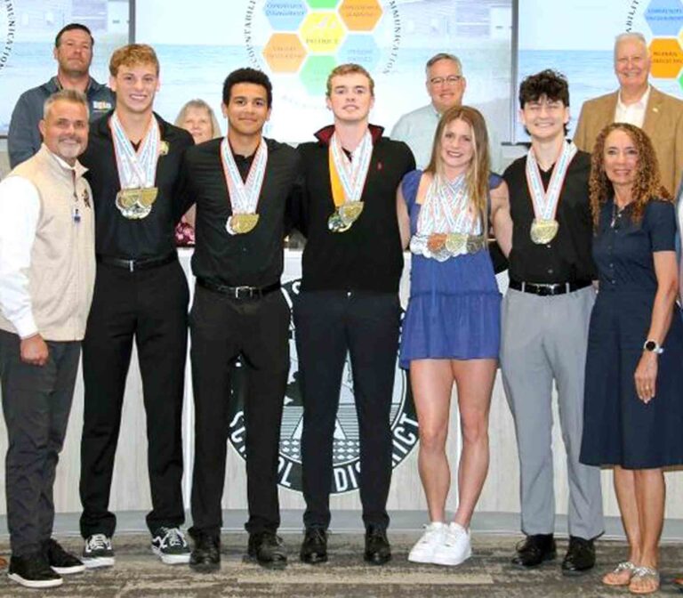 Niceville High School swimmers stand with coaches and officials wearing multiple state championship medals during a school board recognition ceremony.