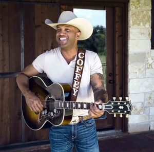 Country singer Coffey Anderson plays guitar while wearing a cowboy hat outdoors