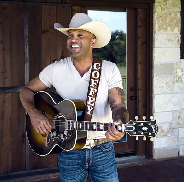 Country singer Coffey Anderson plays guitar while wearing a cowboy hat outdoors