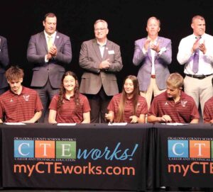 Okaloosa County students sign commitment letters during the 2026 CTE Signing Day ceremony as school officials stand behind them and applaud