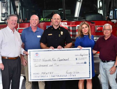 Officials and community leaders present a $10,000 donation check to the Niceville Fire Department in front of a fire engine at the Niceville fire station.