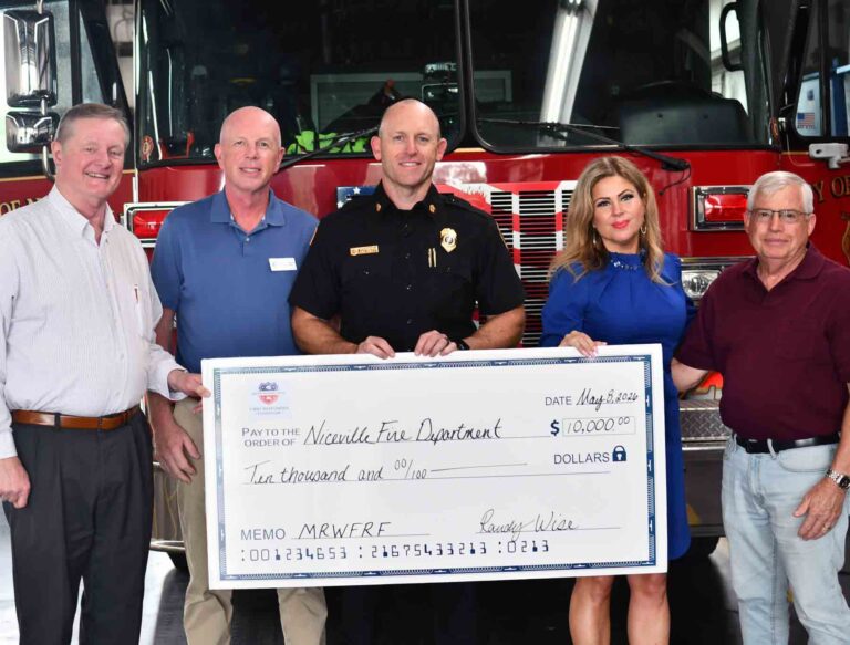 Officials and community leaders present a $10,000 donation check to the Niceville Fire Department in front of a fire engine at the Niceville fire station.