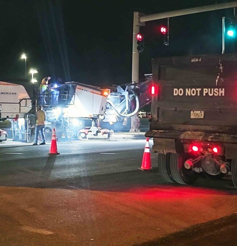 Major traffic shifts, lane closures hit local roads Nighttime road resurfacing work underway at a signalized intersection in Okaloosa County with paving equipment, workers, and traffic cones visible.